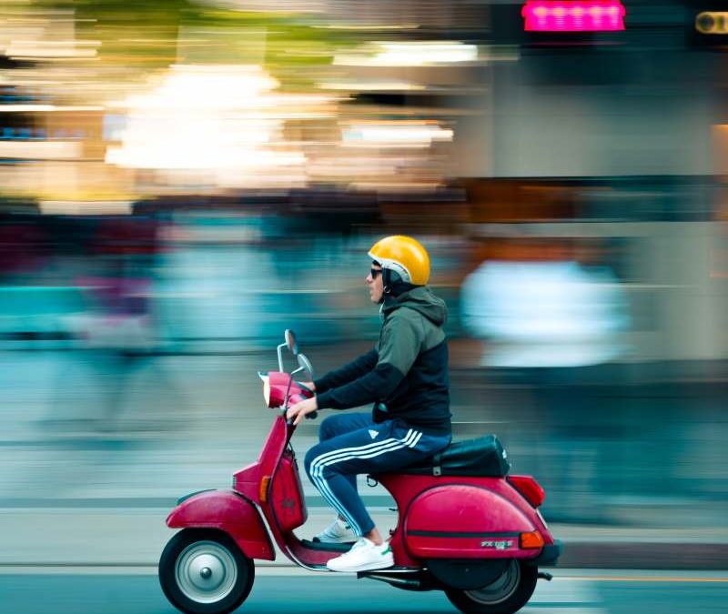 Motorcycle Training Blog Motorcyclist wearing a yellow helmet and sunglasses riding a red scooter, illustrating urban mobility and the excitement of motorcycle adventures.
