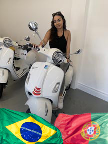 Woman sitting on a white Lexmoto scooter, with Brazilian and Portuguese flags in the foreground, representing the diverse community at North London Motorcycle Training.