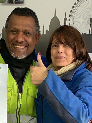 Man and woman smiling and giving a thumbs up, wearing motorcycle training gear, in front of a London skyline backdrop, representing the dedicated office team at North London Motorcycle Training.