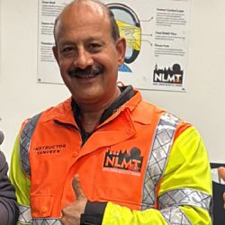 Instructor Tanveer from North London Motorcycle Training (NLMT) wearing a high-visibility jacket, smiling and giving a thumbs-up, representing the dedicated team committed to safe and enjoyable motorcycle training.
