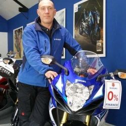 Man in blue jacket standing next to a Lexmoto motorcycle, showcasing motorcycle training environment at North London Motorcycle Training.
