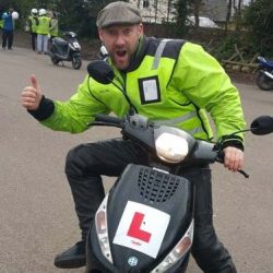 Instructor in high-visibility jacket giving a thumbs-up while seated on a Lexmoto scooter, representing North London Motorcycle Training's commitment to safe and enjoyable motorcycle training.